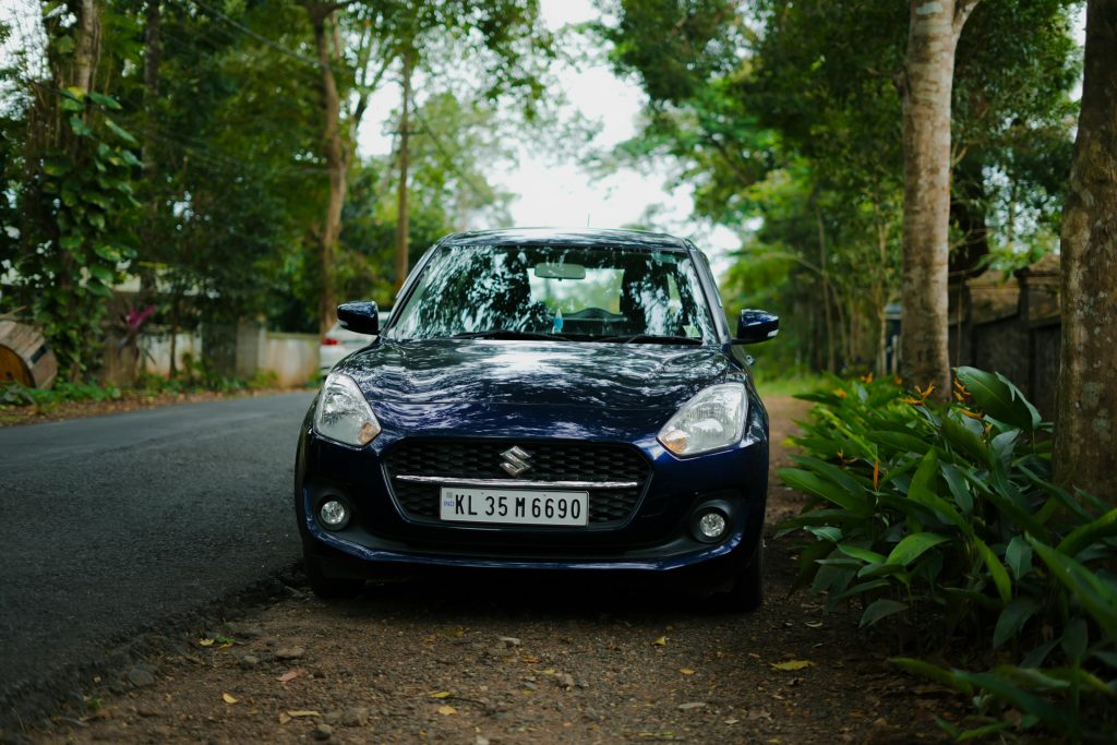 A black compact car parked on a scenic, tree-lined roadside in KL, India.