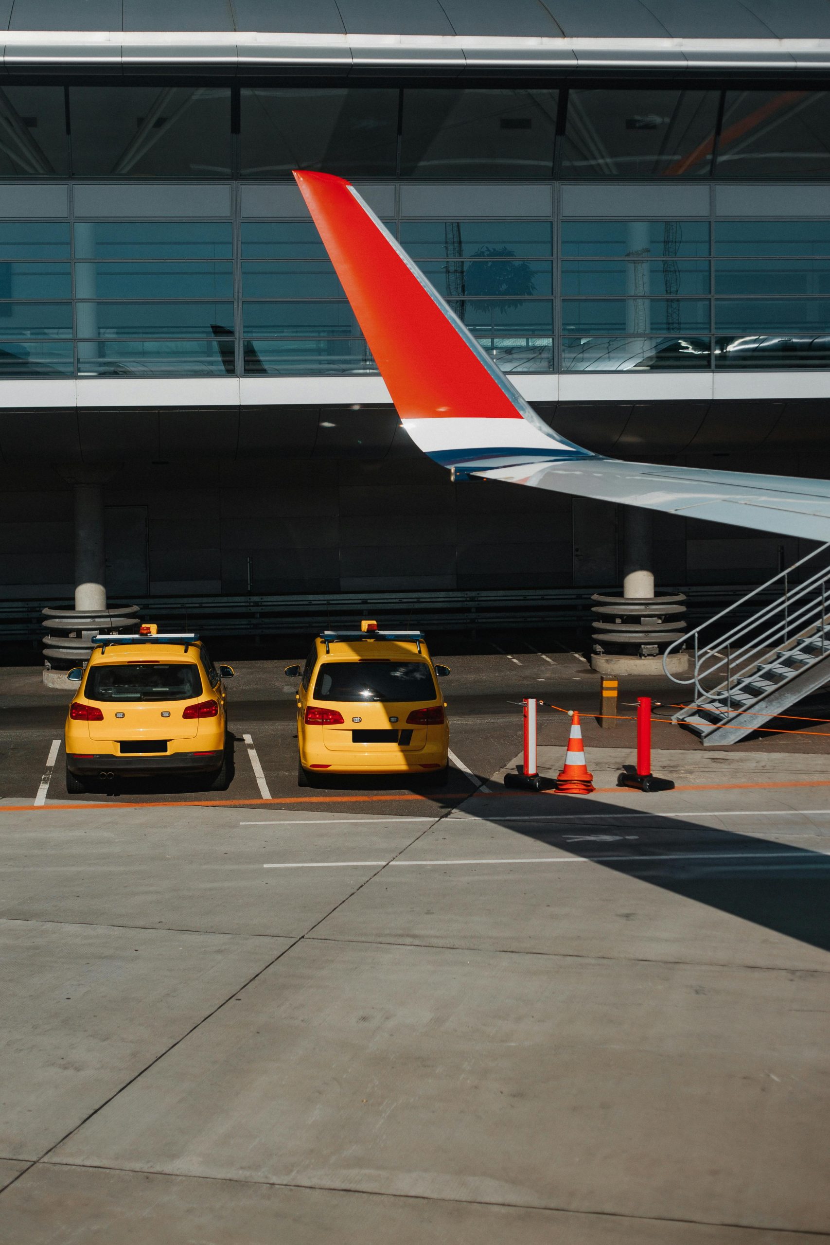 Two yellow taxis parked under an airplane wing at an urban airport.